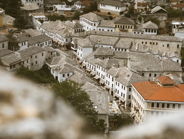 A breathtaking panoramic view of Gjirokastër, a UNESCO World Heritage Site in Albania, featuring its distinctive stone houses with slate roofs, winding cobblestone streets, and the imposing Gjirokastër Castle overlooking the town. Nestled in a lush valley, this historic Ottoman-era town reflects centuries of rich cultural heritage and architectural beauty.